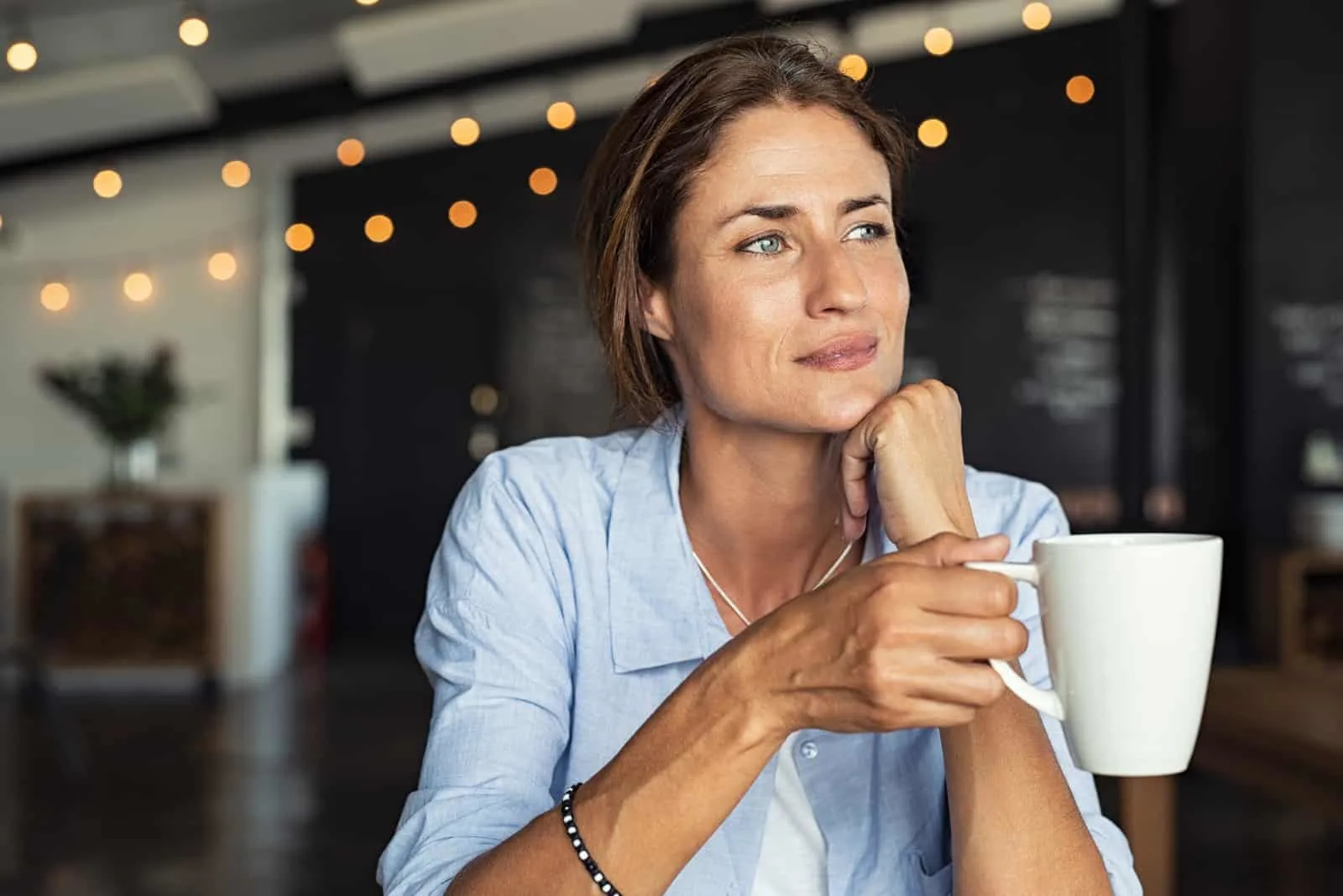 Nachdenkliche reife Frau, die in der Cafeteria mit Kaffee sitzt holding