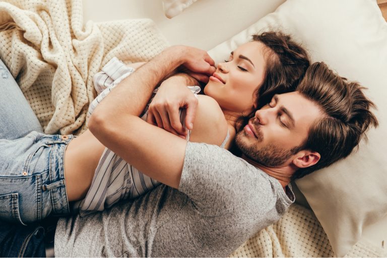 Schönes glückliches junges Paar, das sich beim Schlafen auf dem Bett umarmt