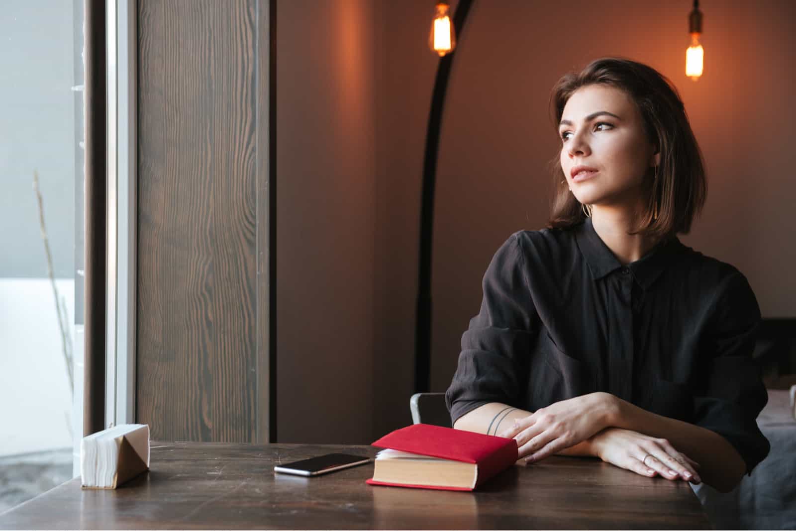 glückliche junge Frau, die am Tisch in der Nähe von Buch sitzt sitting