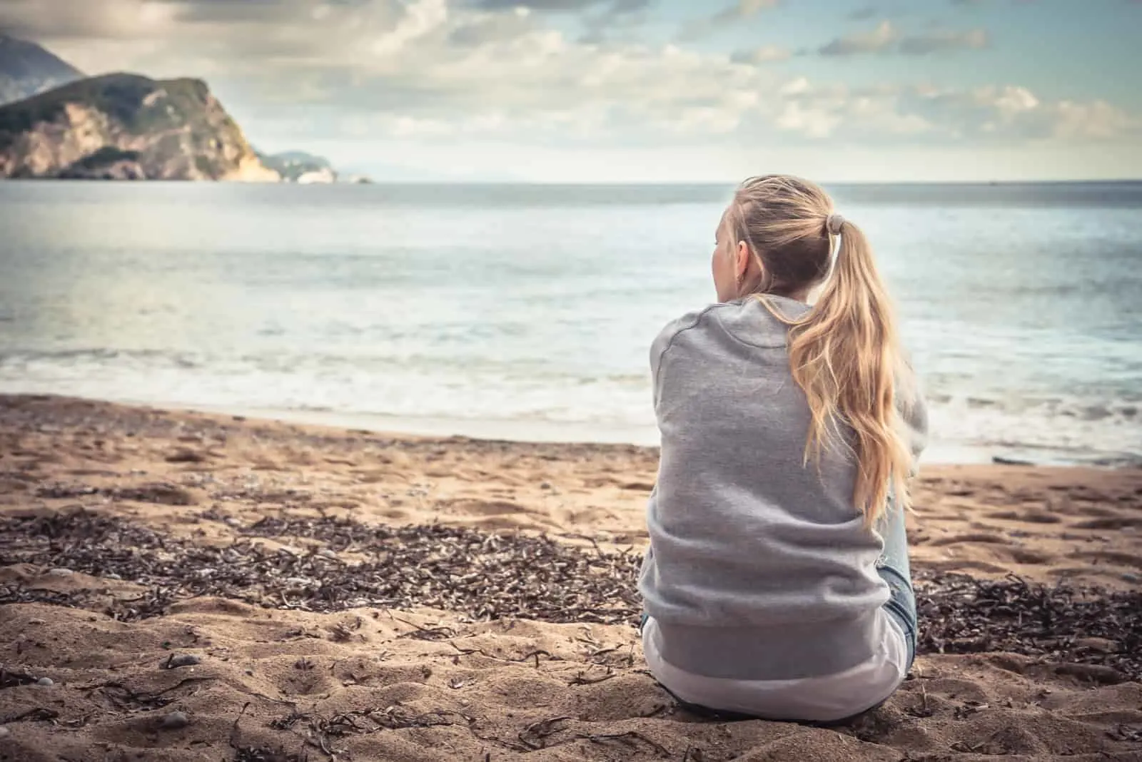 junge Frau sitzt am Strand und umarmt ihre Knie