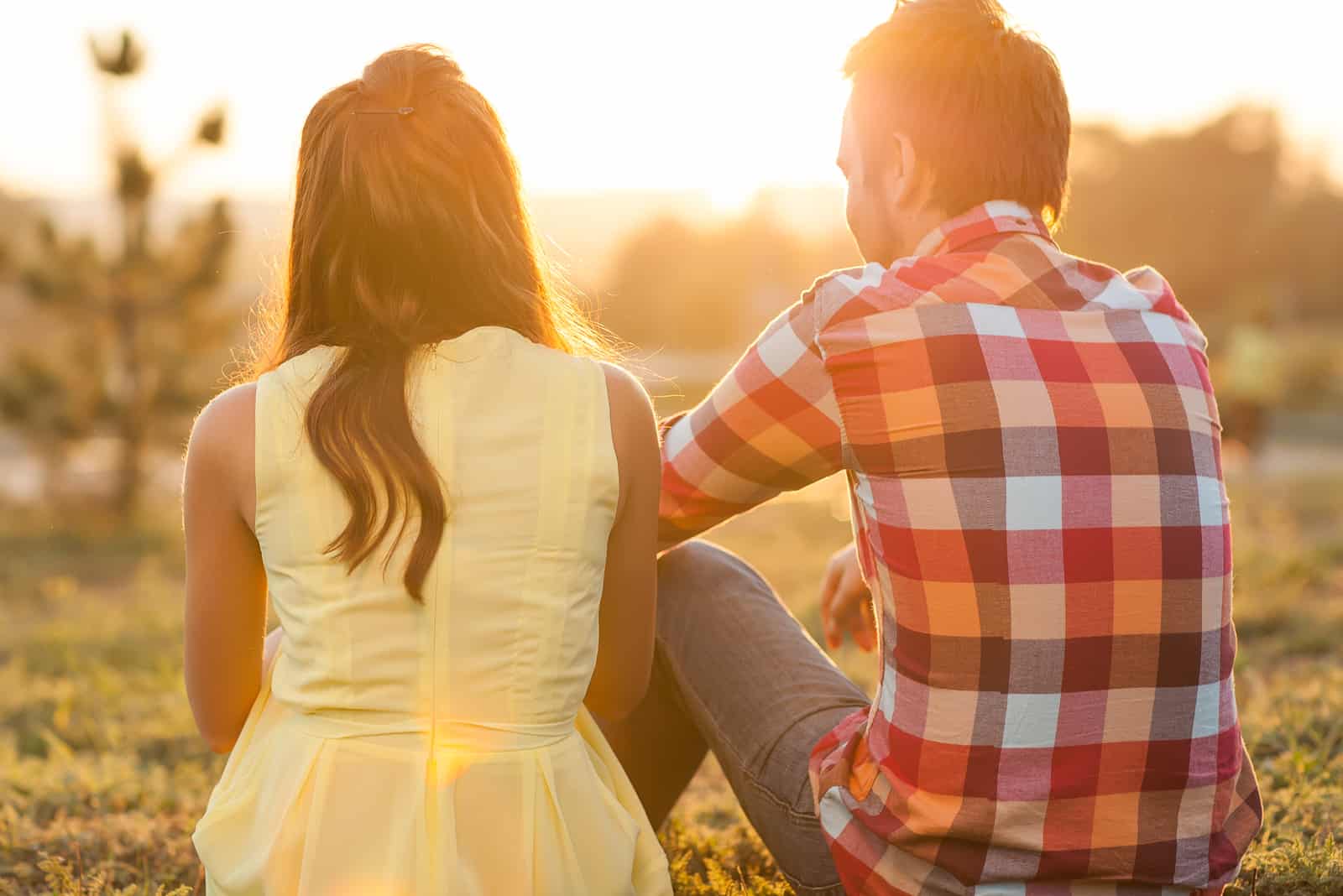 junges glückliches Paar, das bei Sonnenuntergang auf dem Gras sitzt