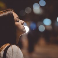 Junge schöne Frau, die sich in der Stadt in Seitenansicht auf eine Straßenlaterne stützt