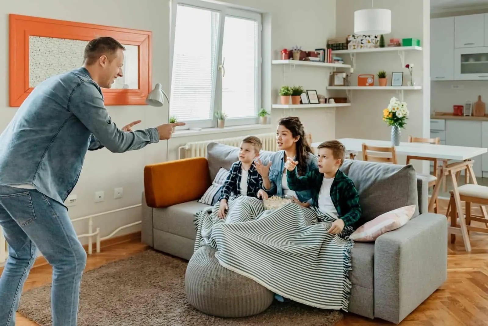 Familie spielt Ratespiel im Wohnzimmer mit dem Vater, der vor der Mutter und den Kindern steht