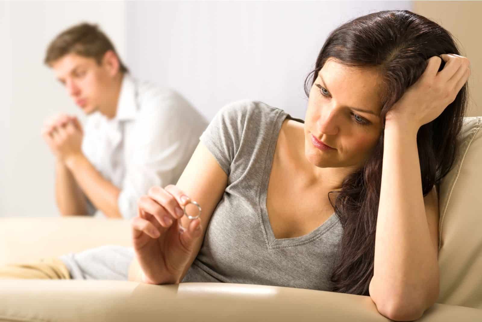 Frau schaut auf den Ring beim Gedanken an die Trennung vom weit sitzenden Ehemann