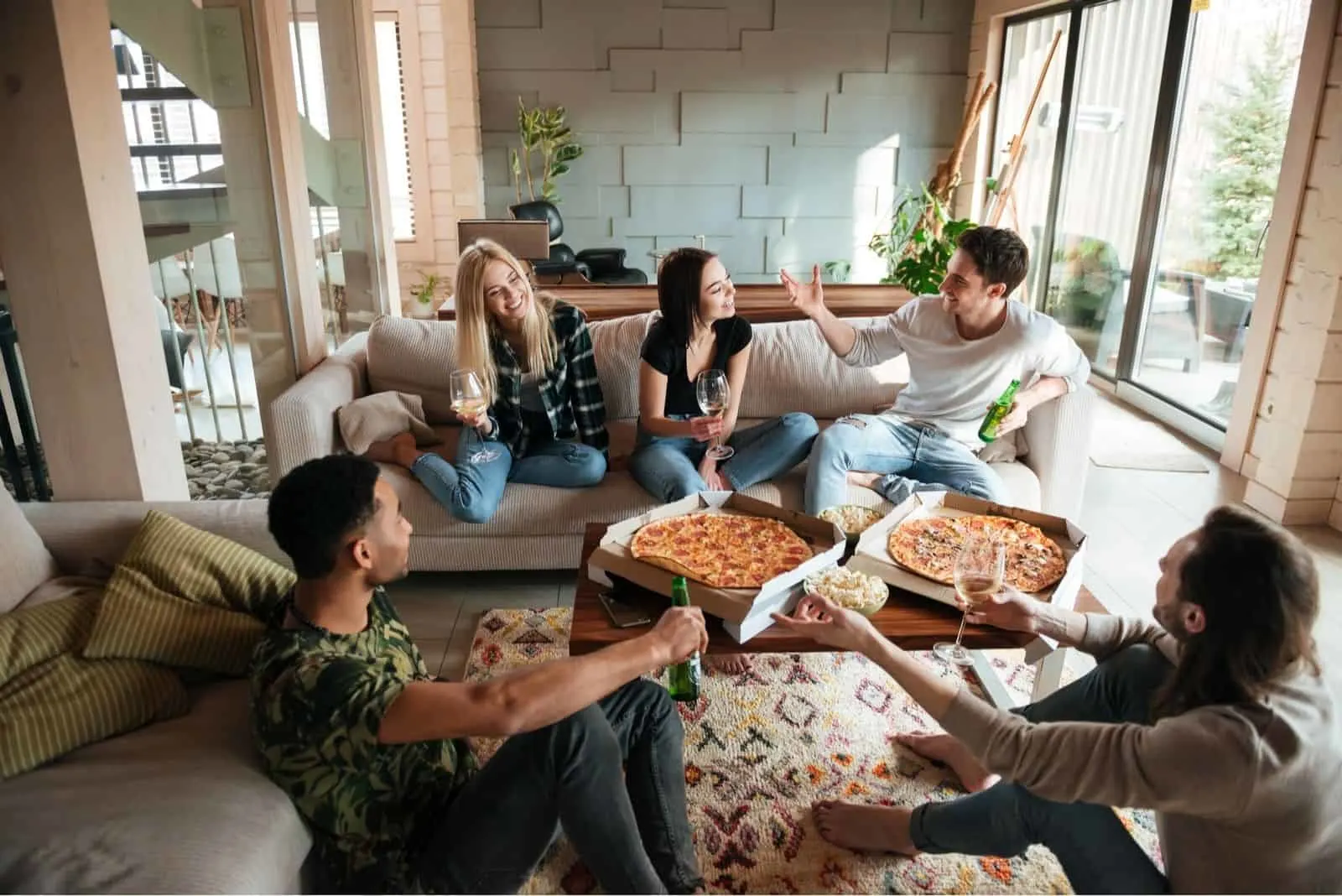 Gruppe junger fröhlicher Freunde eine gute Zeit beim Pizza- und Bieressen im Wohnzimmer haben