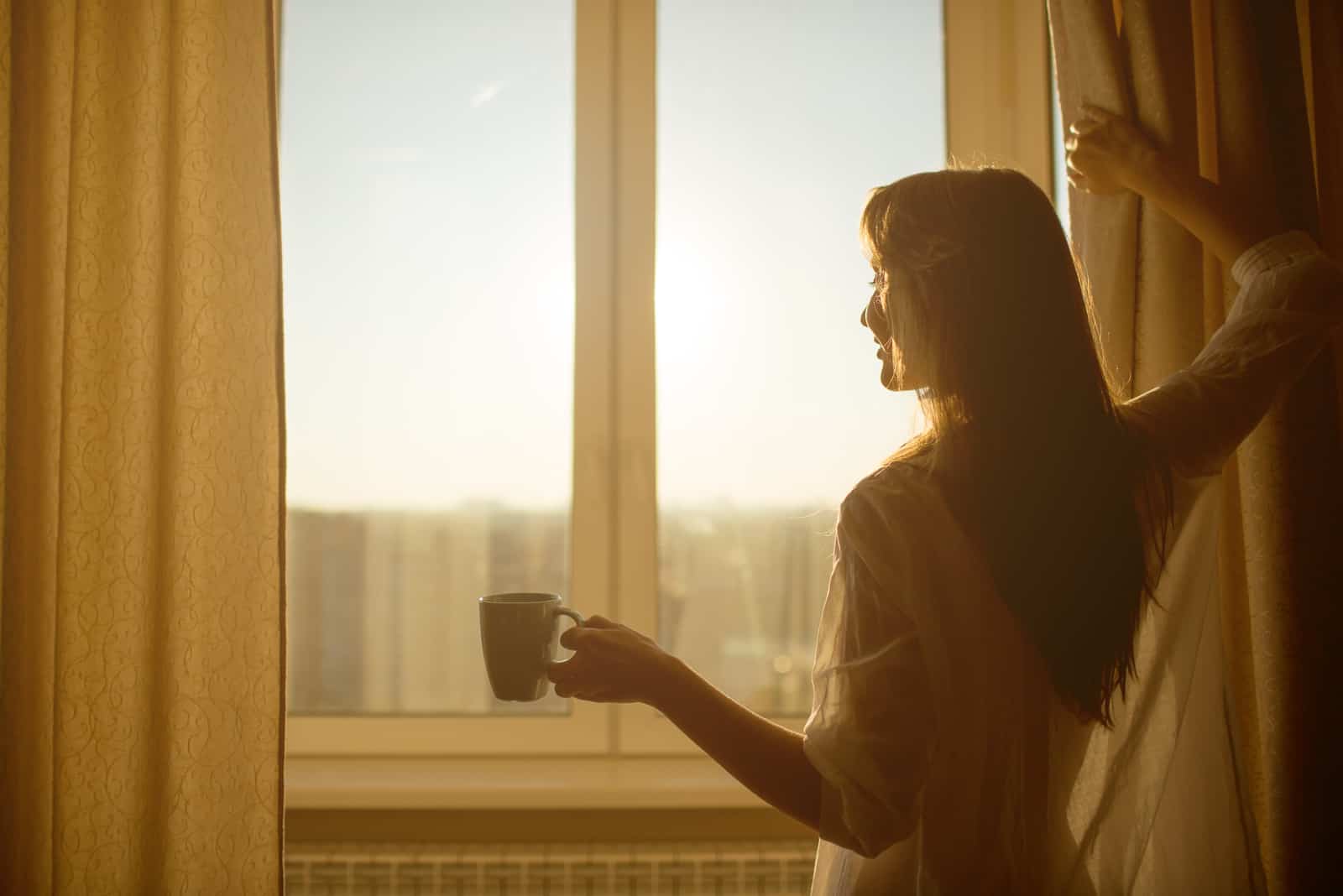 Frau schaut morgens aus dem Fenster
