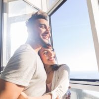 Junges Paar umarmt moderne Wohnung mit großem Panoramafenster mit Meerblick