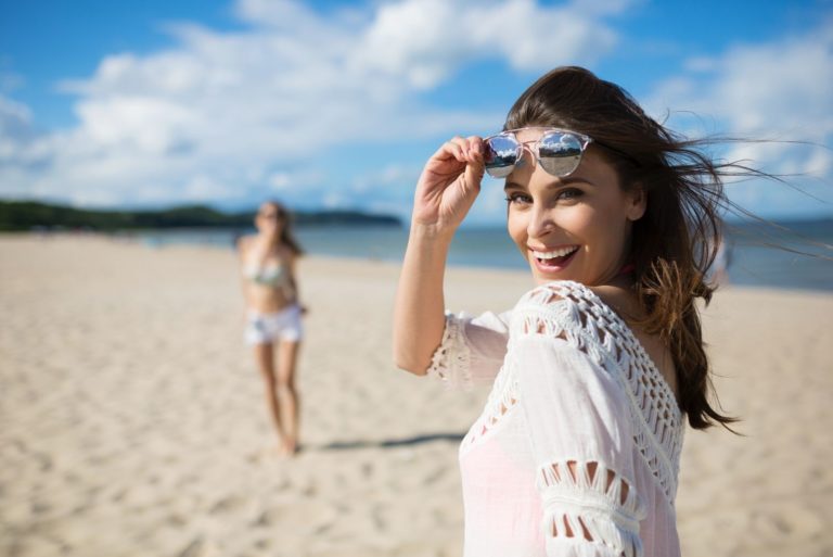 glückliche schöne Frau, die am Strand spazieren geht und zurück in die Kamera schaut