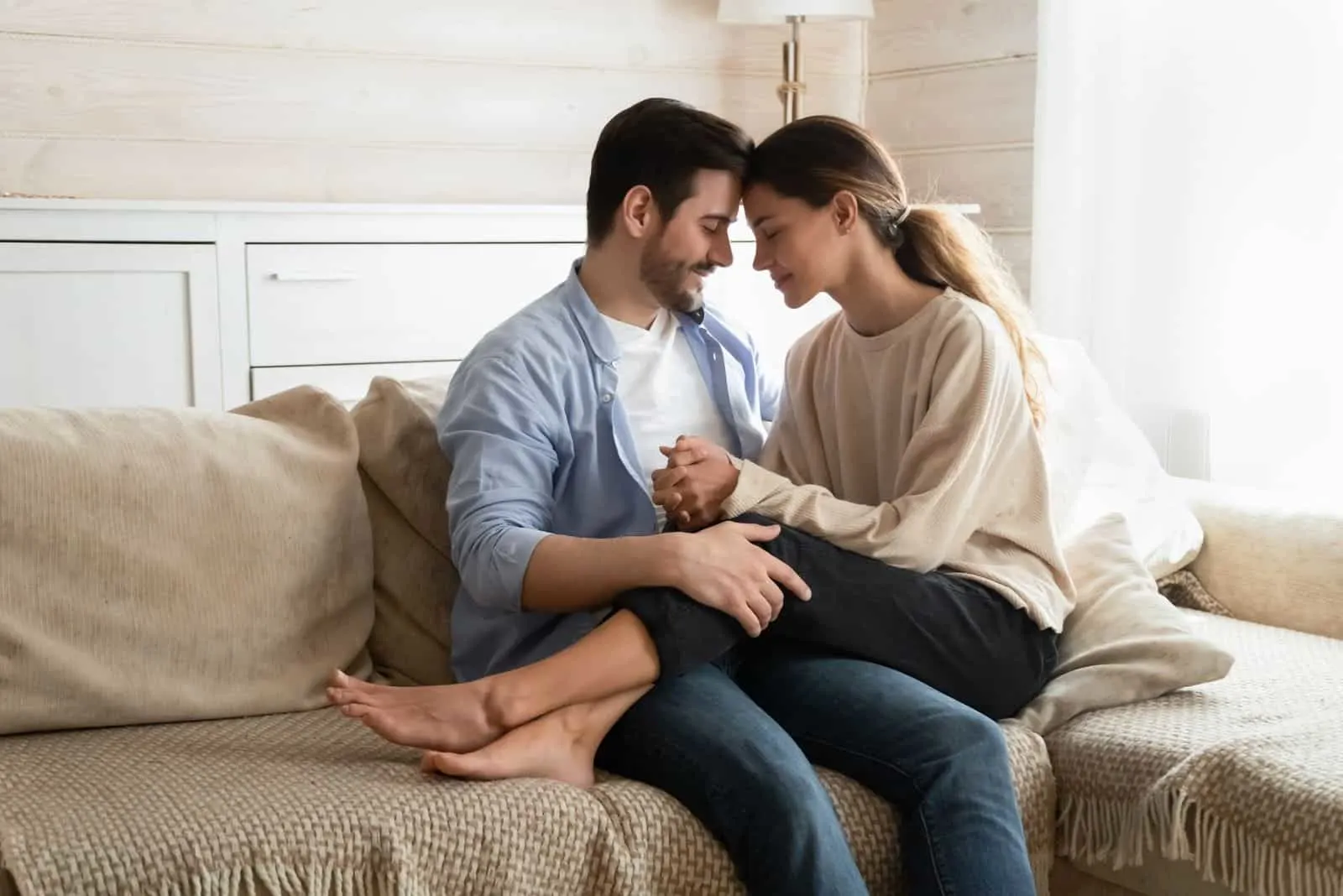 Liebevolles junges Ehepaar auf der Couch im Wohnzimmer sitzen und kuscheln kuscheln zärtlich süßen Moment zusammen genießen