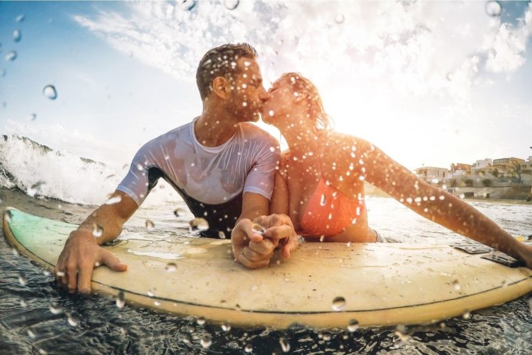 Glückliches sportliches Paar, das sich beim Surfen im Meer küsst