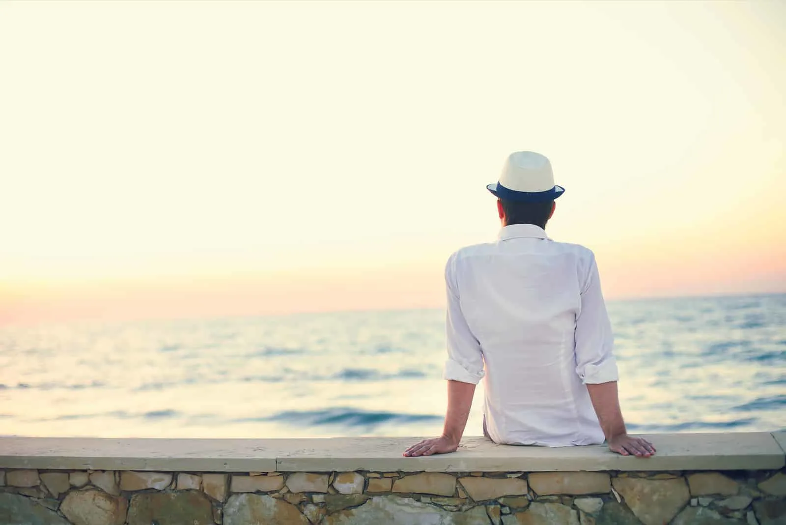 ein Mann mit Hut auf dem Kopf sitzt und schaut aufs Meer