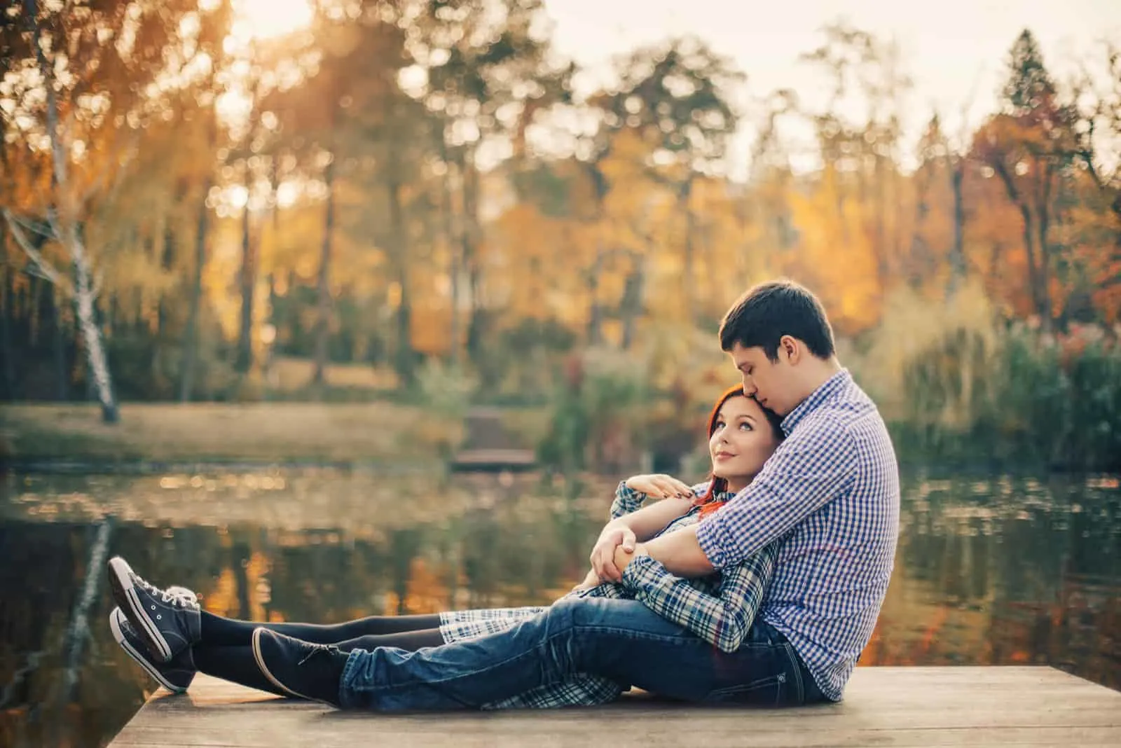 ein Mann und eine Frau sitzen sich umarmend auf einem Pier am Fluss