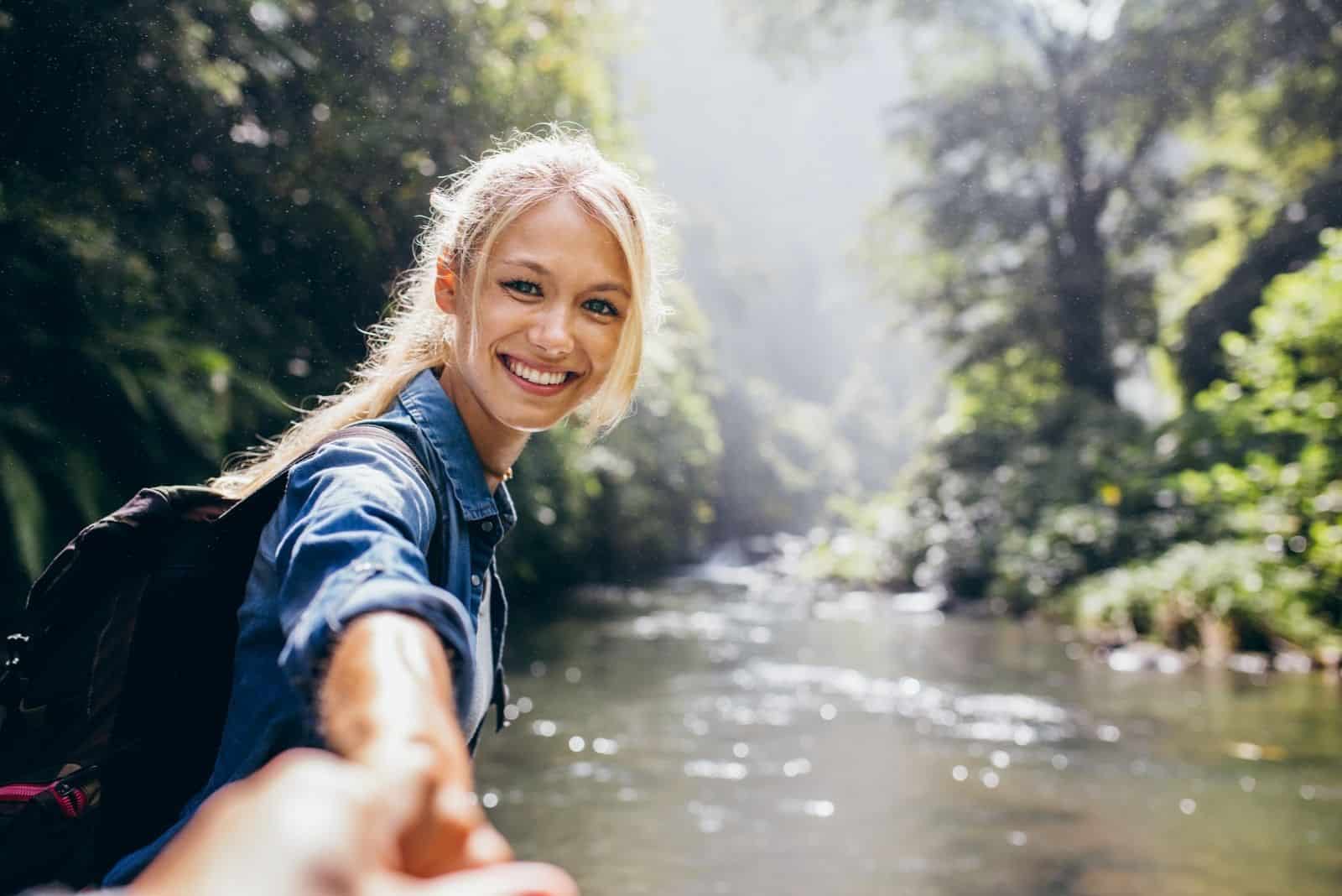glückliche junge Frau, die Hand hält ihres Freundes beim Wandern am Gebirgsbach.