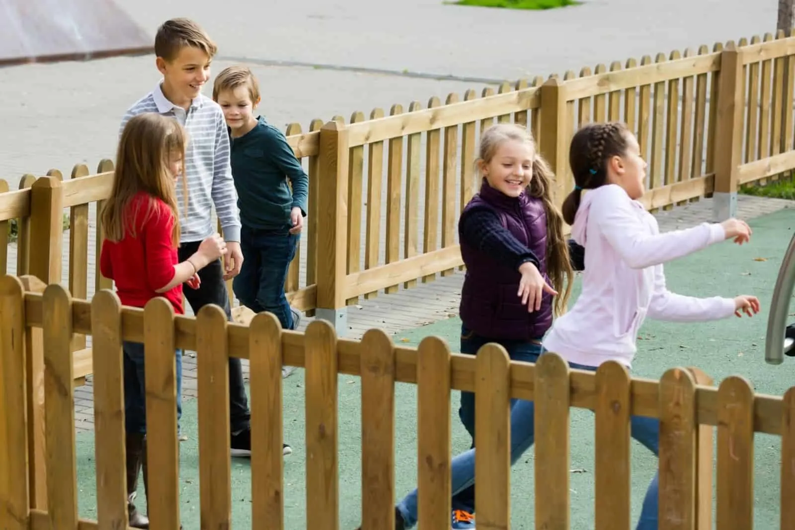 glückliche spielende Kinder innerhalb eines Zauns im Freien fangen und berühren