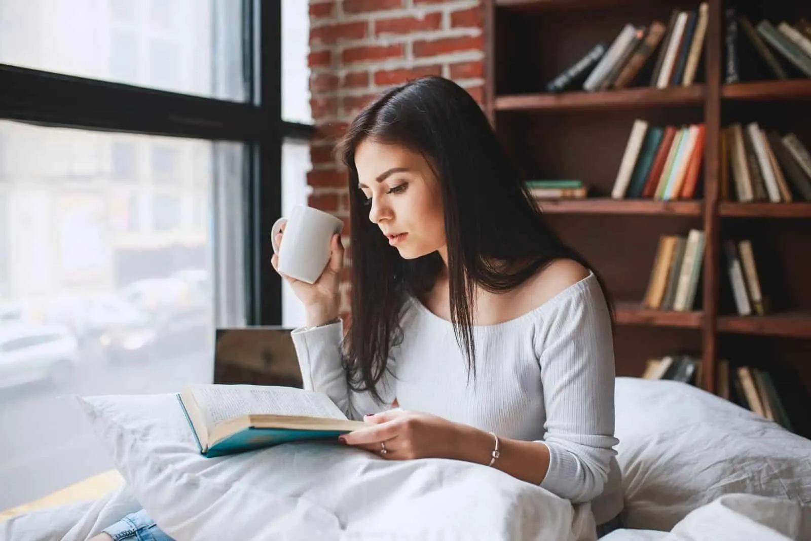 hübsche Frau liest Buch im Wohnzimmer mit einer Tasse Kaffee