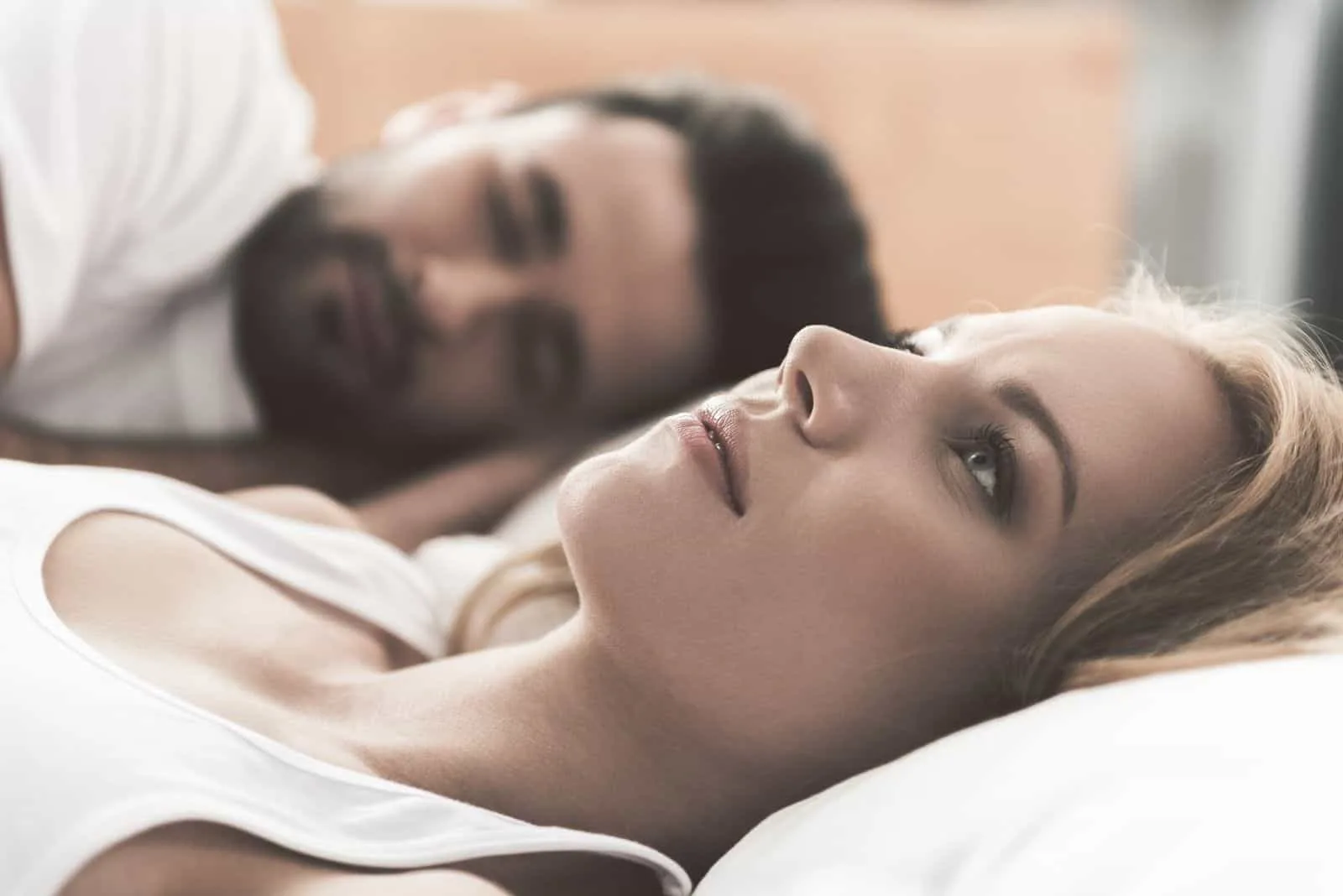 junge Frau macht sich Sorgen über ihre Ehe wach neben dem schlafenden Ehemann liegen