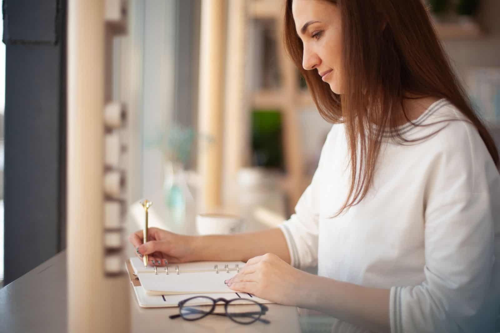 junge Geschäftsfrau mit Brille auf dem Tisch auf einen Planer schreiben