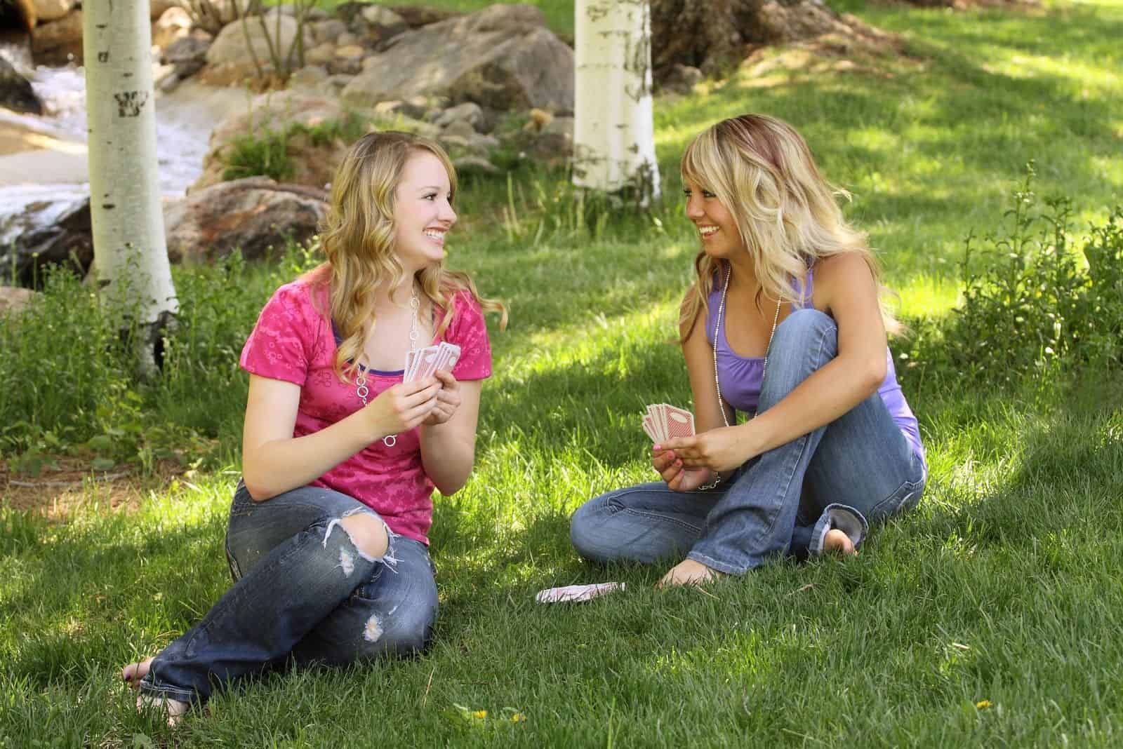 zwei Freundinnen Kartenspielen im Park auf dem Boden sitzend
