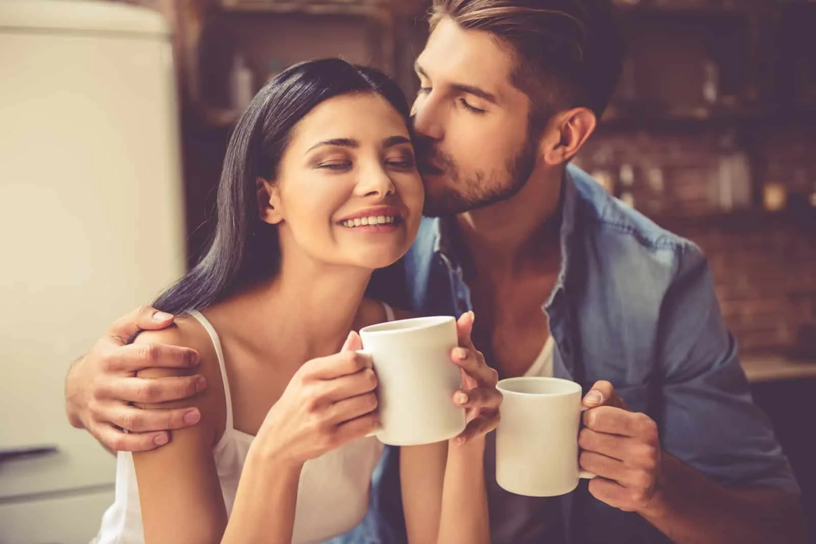 Ein Mann küsst eine Frau beim Kaffeetrinken auf die Stirn