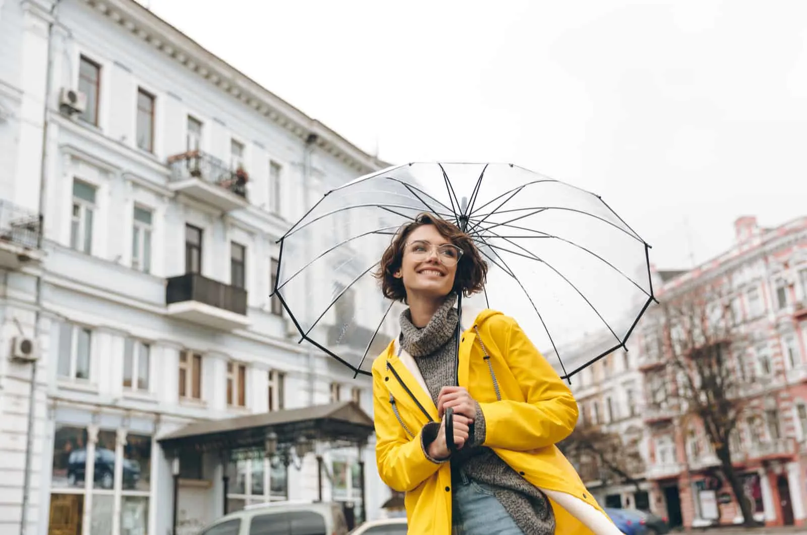 lachelnde junge frau in einem gelben regenmantel und einem regenschirm