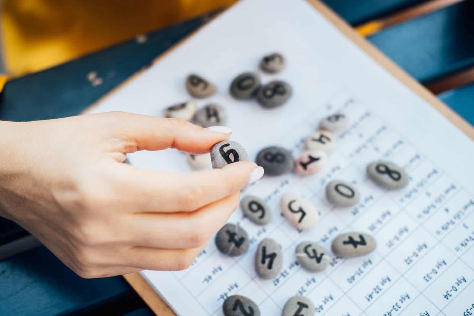 Frau hält einen Kieselstein mit handgemalter Lebenszahl 6