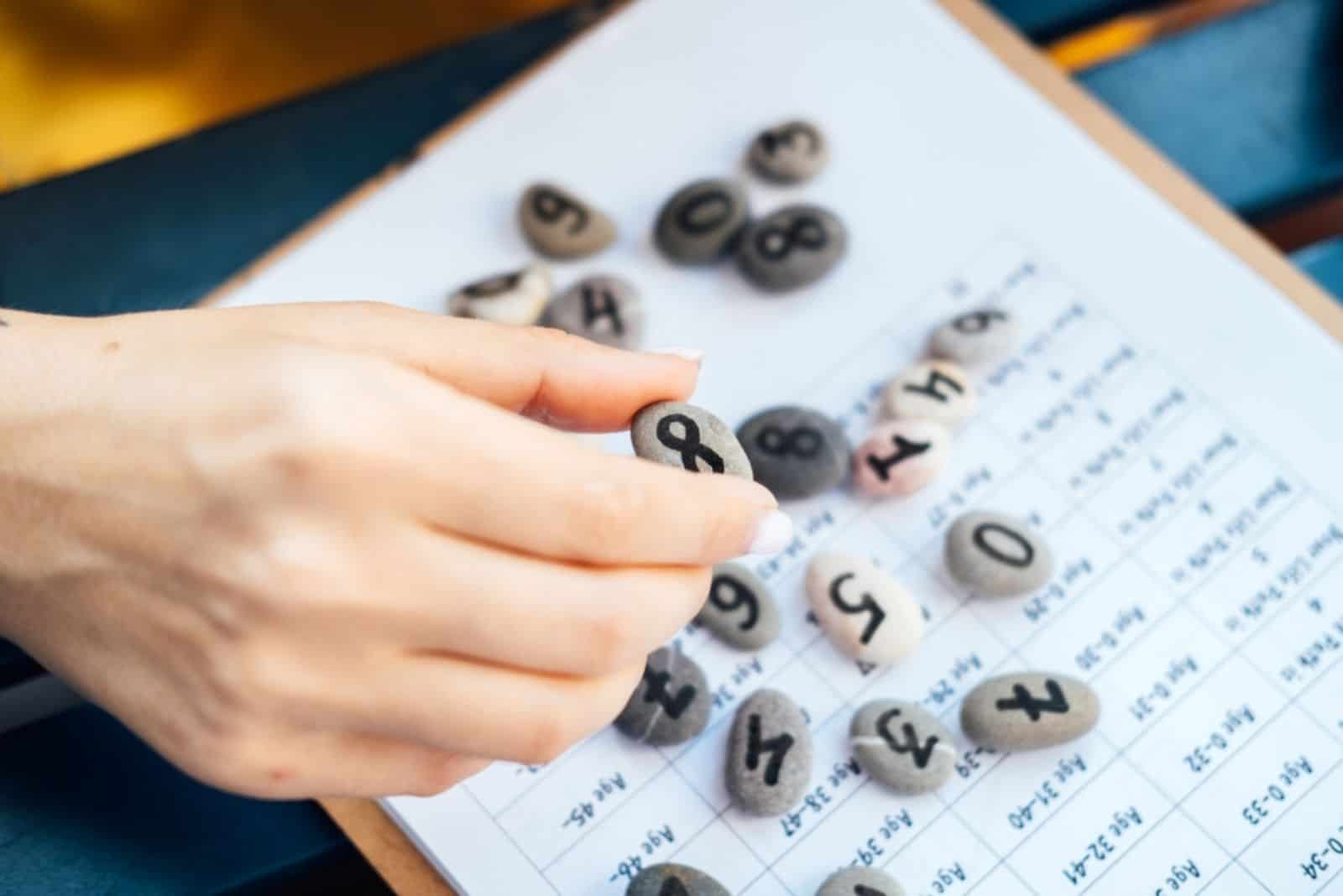 Frau hält einen Kieselstein mit handgemalter Lebenszahl 8