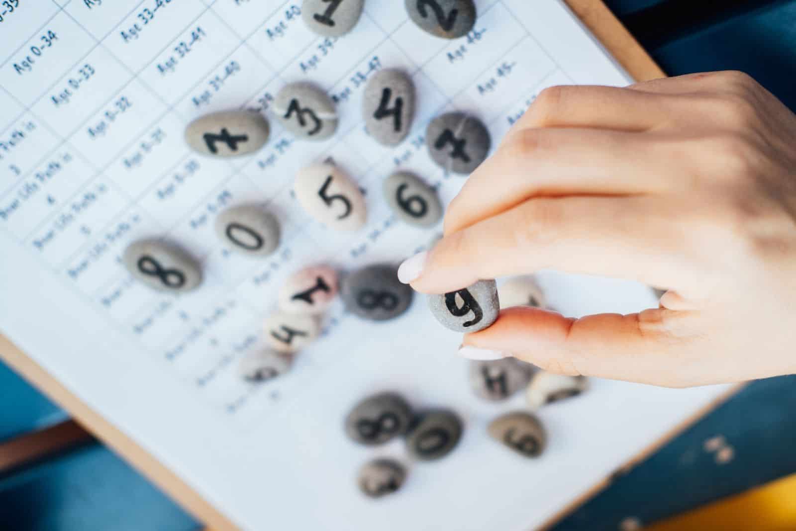 Frau hält einen Kieselstein mit handgemalter Lebenszahl 9