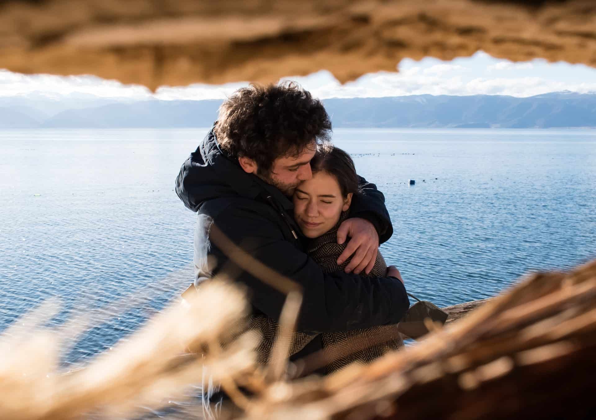 Mann umarmt Frau mit Meer im Hintergrund