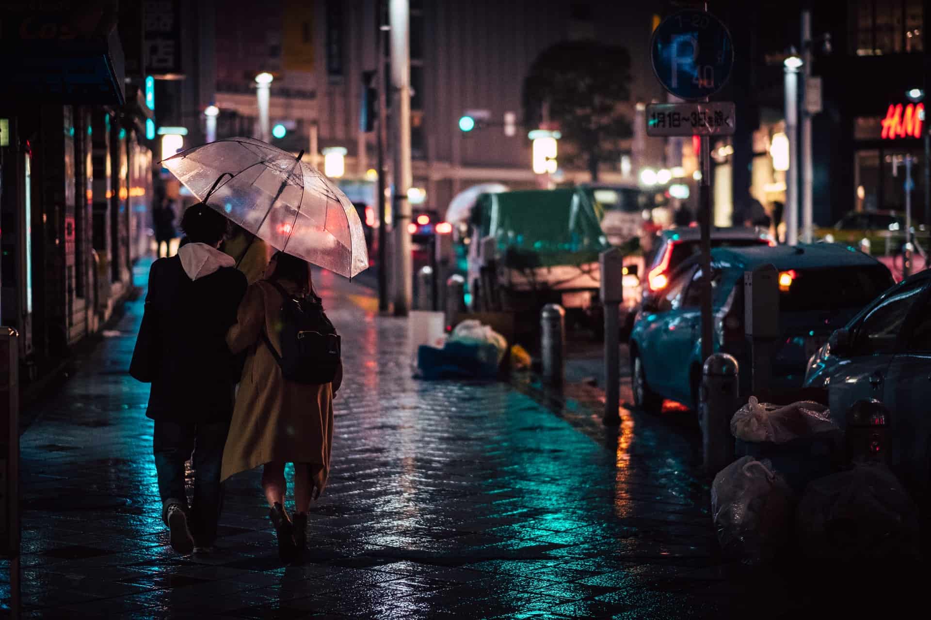 Paar geht mit Regenschirm auf einer verregneten Straße