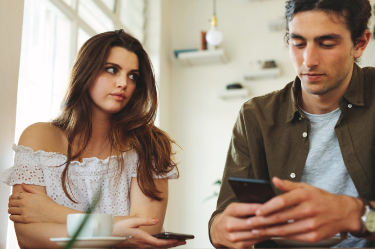 Frau macht sich Sorgen um ihren Partner, der auf das Telefon schaut