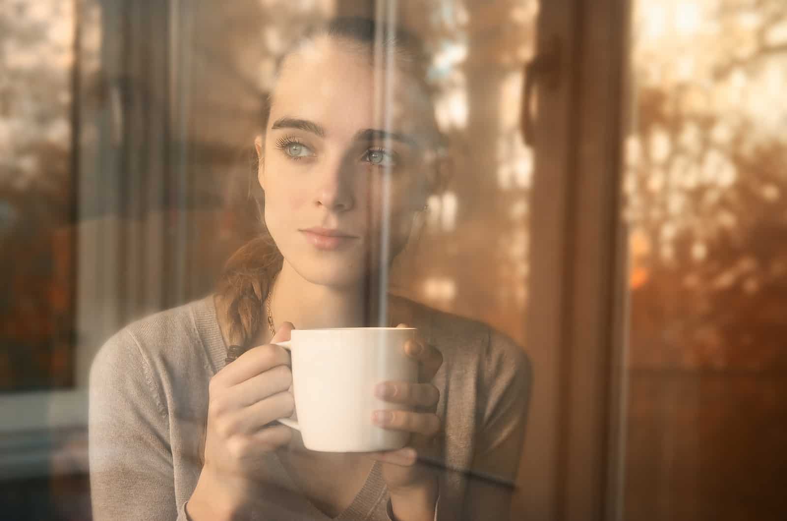 Traurige Frau, die Kaffee trinkt und aus dem Fenster schaut