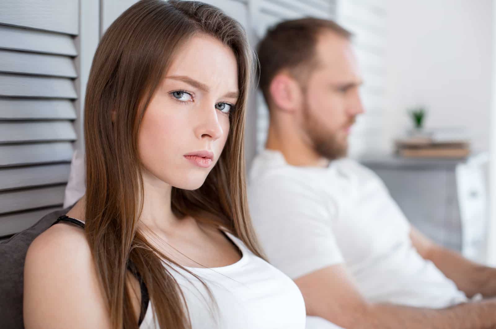 Unzufriedene Frau sitzt neben ihrem Partner und schaut in die Kamera