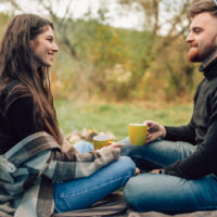 Ein lächelnder Mann und eine Frau sitzen unter einem Zelt, trinken Kaffee und unterhalten sich