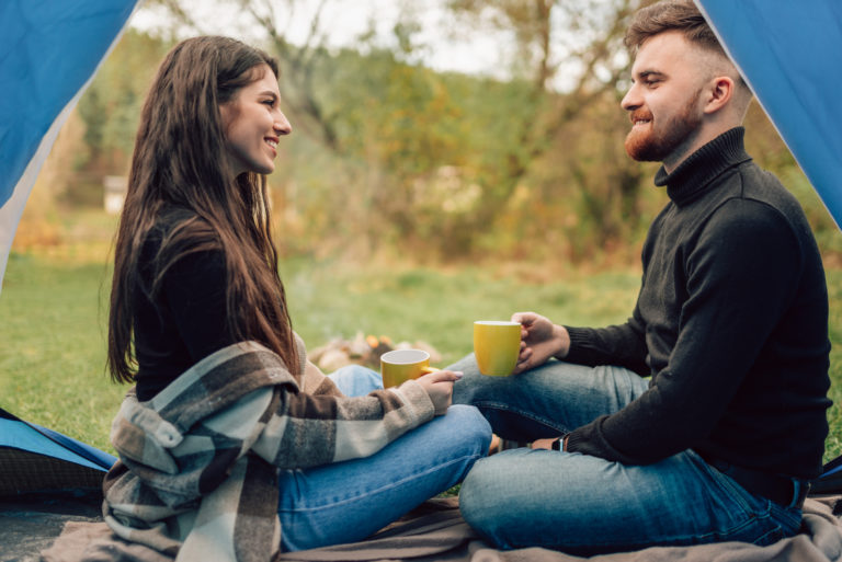 Ein lächelnder Mann und eine Frau sitzen unter einem Zelt, trinken Kaffee und unterhalten sich