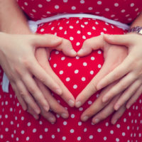männliche und weibliche Hände bilden ein Herz auf einem schwangeren Bauch
