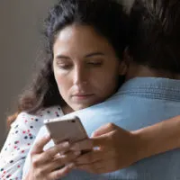 Frau, die auf das Telefon schaut, während sie ihren Freund umarmt