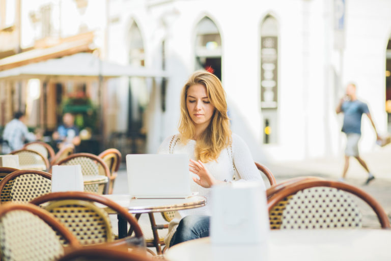 Frau im weißen Hemd, die draußen im Café arbeitet