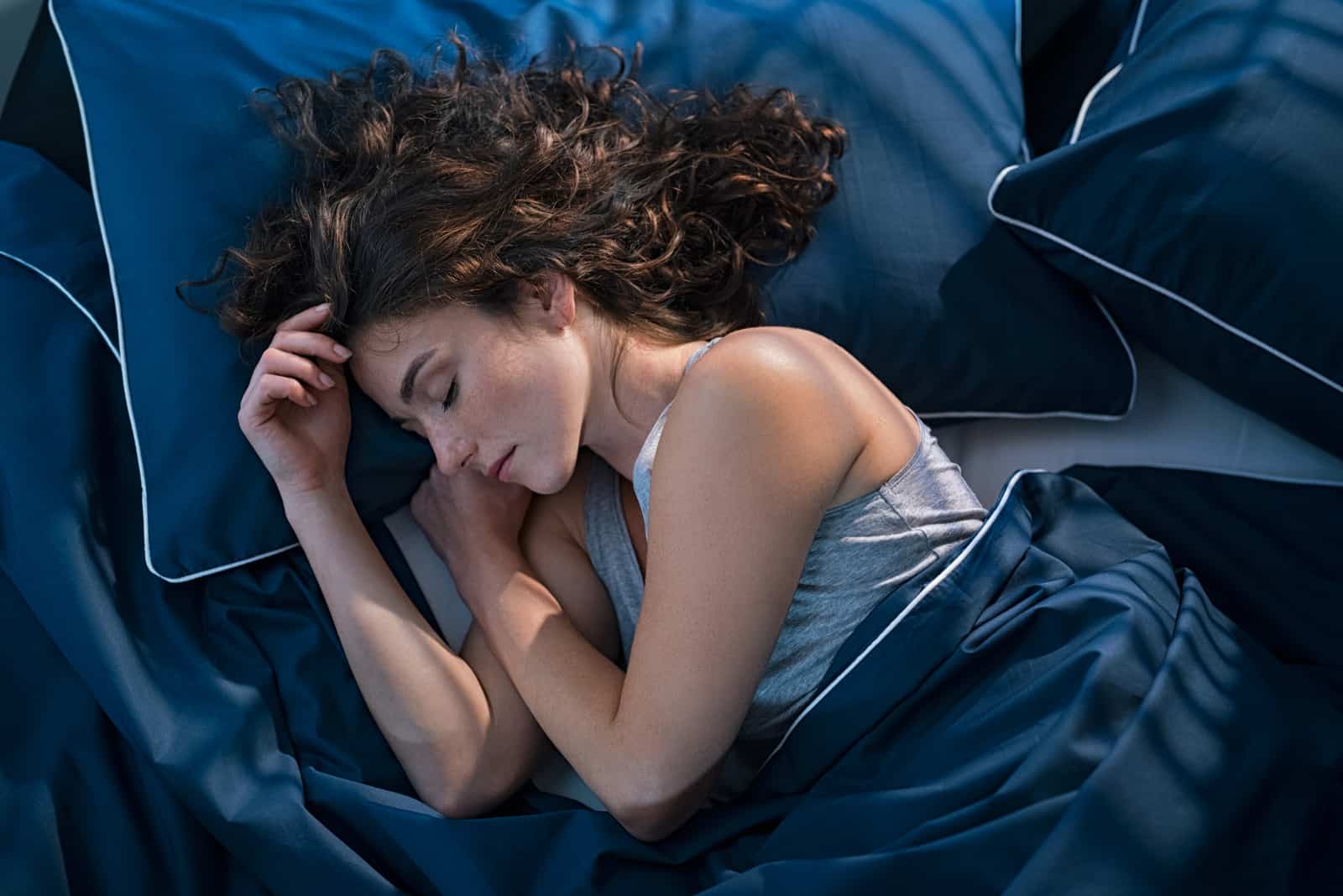 Frau schläft auf Bett mit dunkelblauen Laken