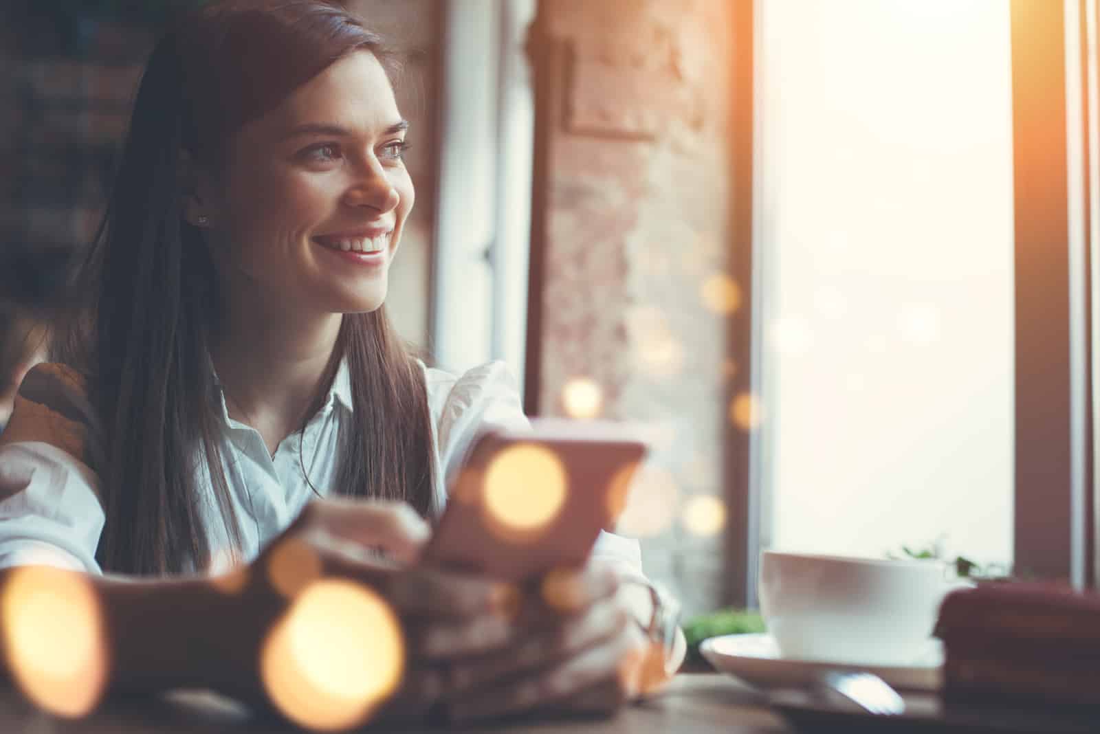 Lächelnde Frau im Café mit Handy und SMS