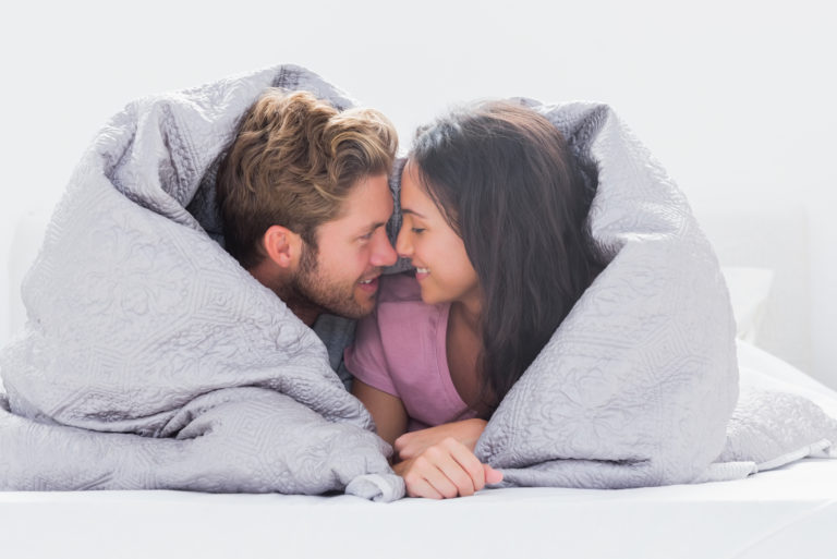 Paar kuschelt unter der Decke auf dem Bett