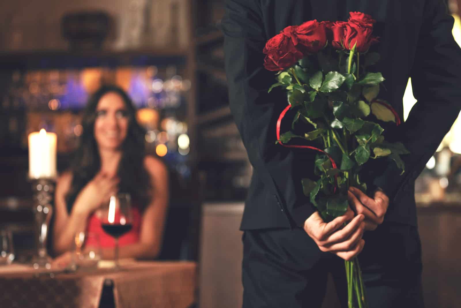 Mann versteckt Rosen für Frau beim Abendessen