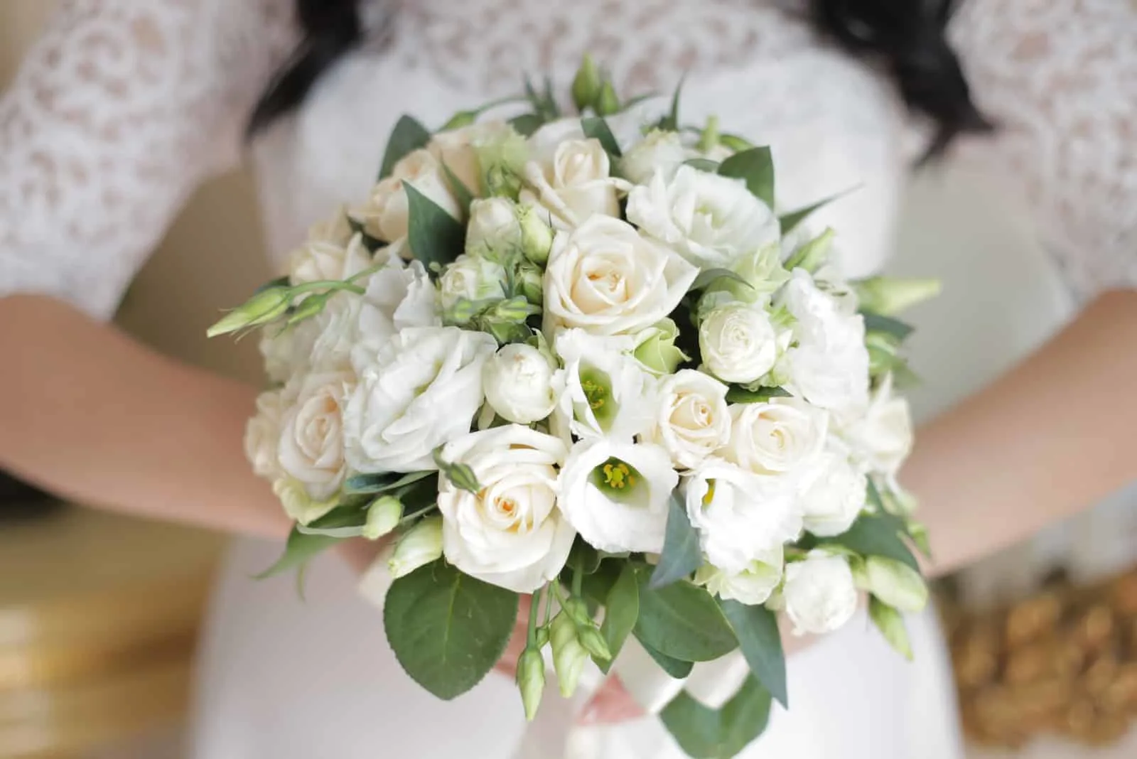 die Braut hält einen Brautstrauß aus weißen Rosen und Eustoma