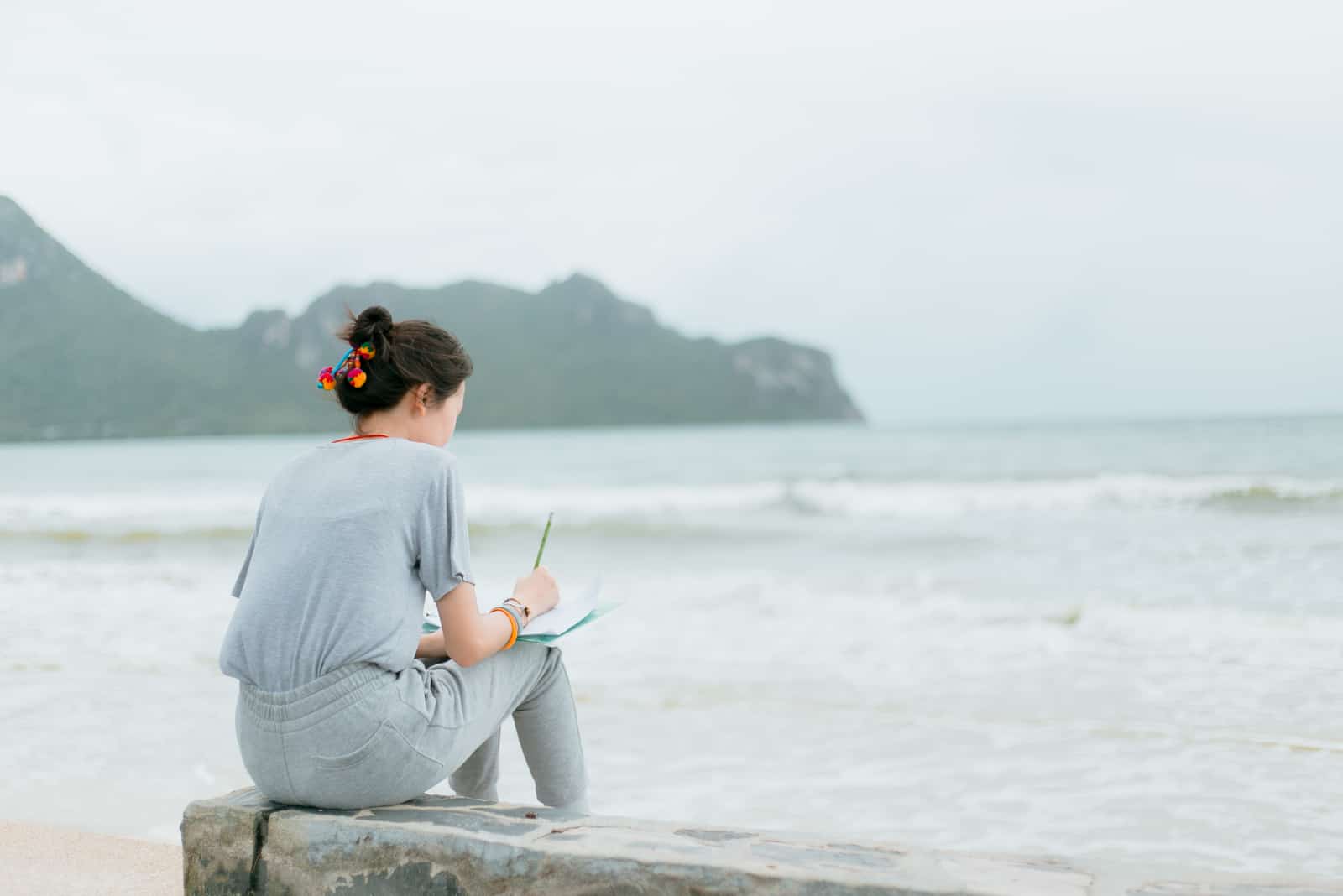 Frau, die auf einem Felsen am Meer sitzt und einen Brief schreibt