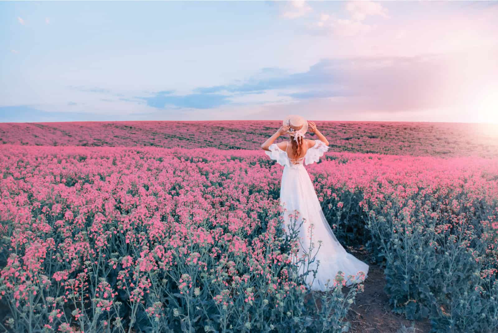 Frau mit rosa Hut steht in einem rosa Blumenfeld