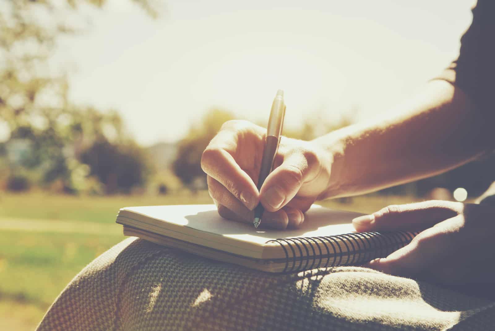 Frau sitzt im sonnigen Park und schreibt einen Brief