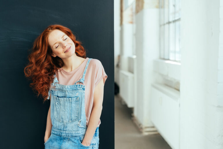 Lächelnde junge Frau mit einem glücklichen, ruhigen Lächeln, die trendige Denim-Latzhosen trägt