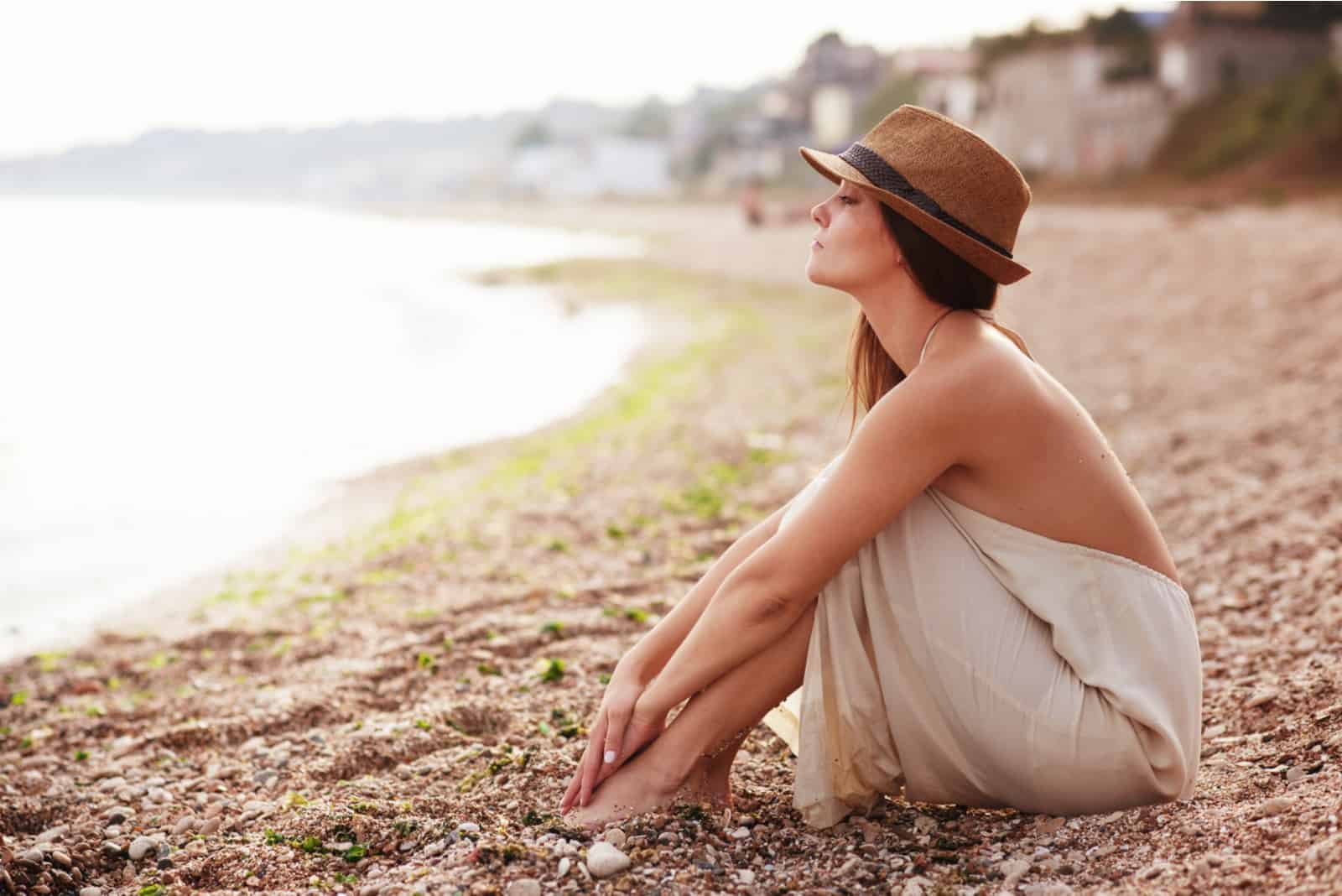 Eine Frau mit Hut auf dem Kopf sitzt am Strand