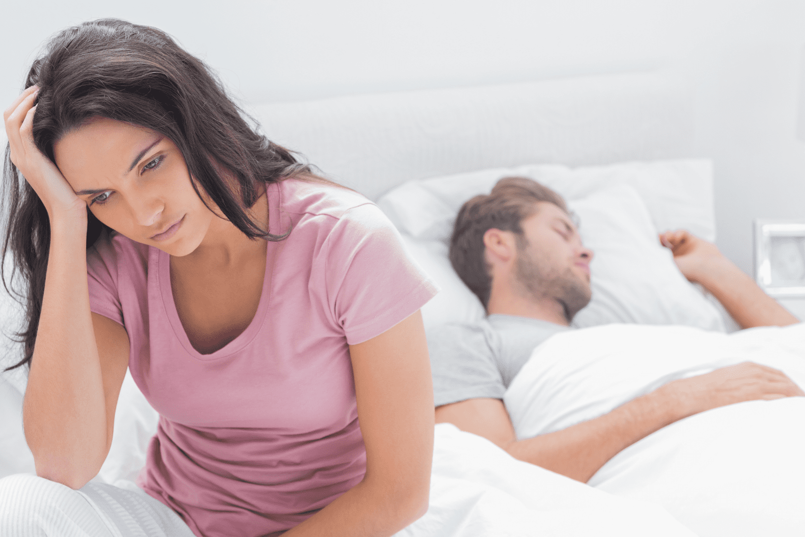 Die Frau sitzt auf dem Bett, während der Mann schläft