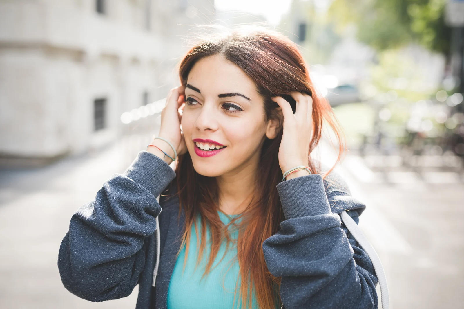Eine lächelnde Frau mit langen braunen Haaren hält ihr Ohr