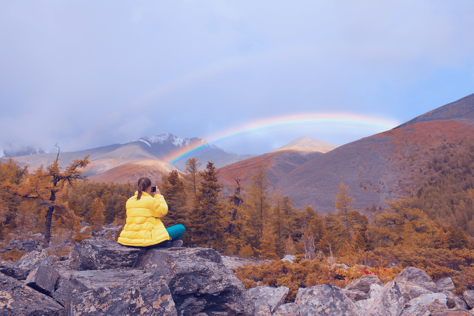 Eine Frau sitzt auf einem Felsen und malt einen Regenbogen